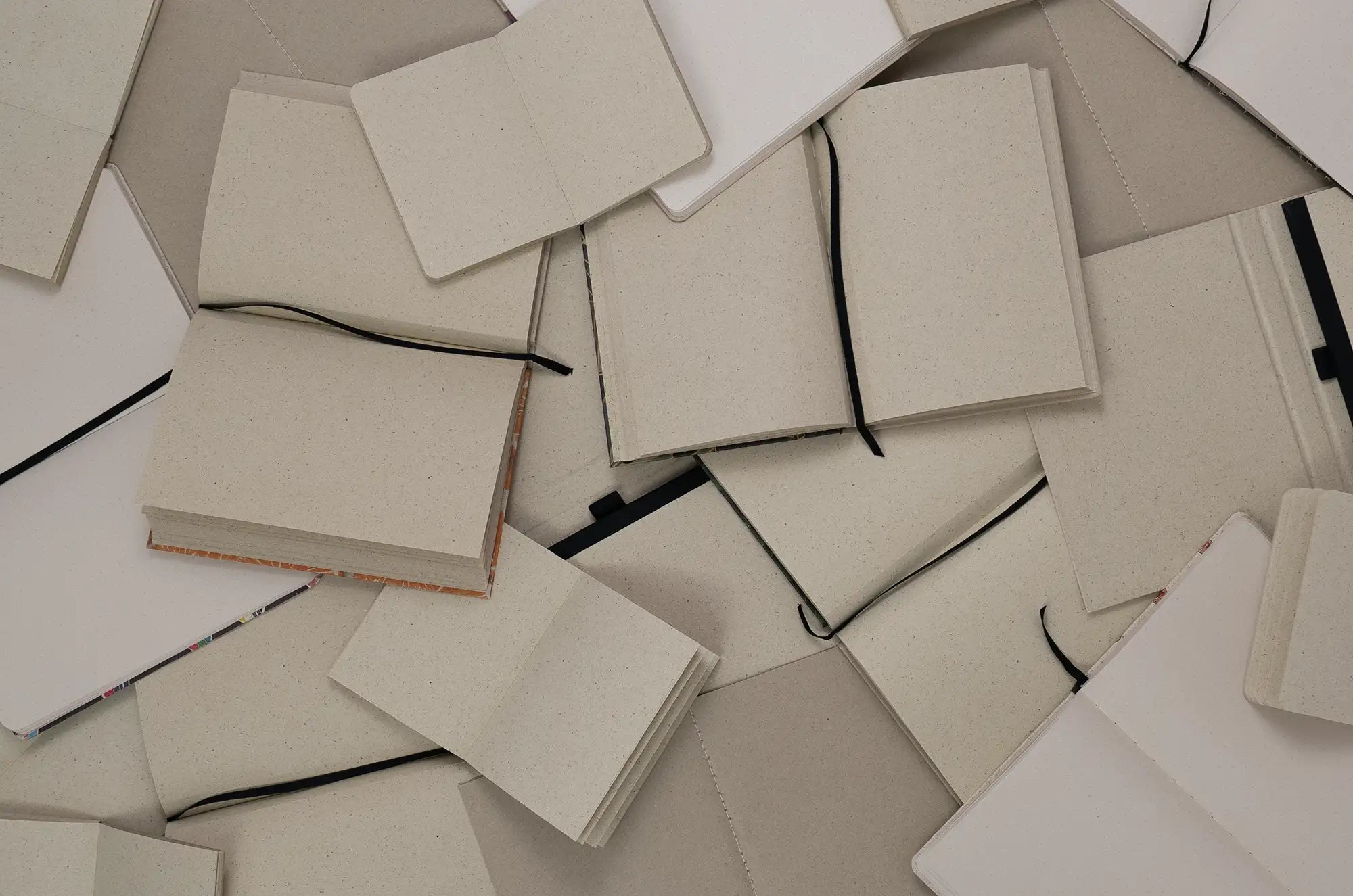 Vegan produzierte Notizbücher, Postkarten, Papierprodukte, Schreibwaren und Geschenkideen liegen aufgeschlagen durcheinander aus Graspapier von matabooks