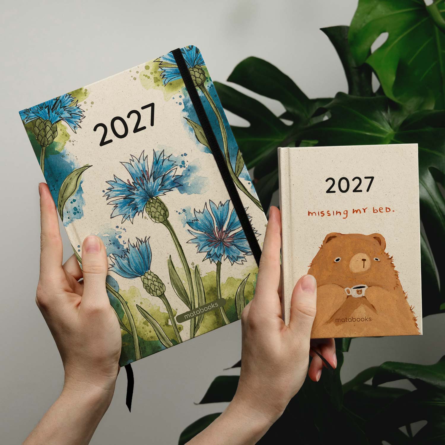 Zwei vegan produzierte Jahresplaner, Jahreskalender, Kalender, Familienkalender, Notizbuch, Tagebuch, Terminplaner, Achtsamkeitstagebuch, Bullet Journal, Reisetagebuch, Dankbarkeitstagebuch, Hausaufgabenheft, Uni-Planer, Taschenkalender, Buchkalender, Business-Planer, Wochenplaner A5 und A6 aus Graspapier von matabooks vor floralem Hintergrund